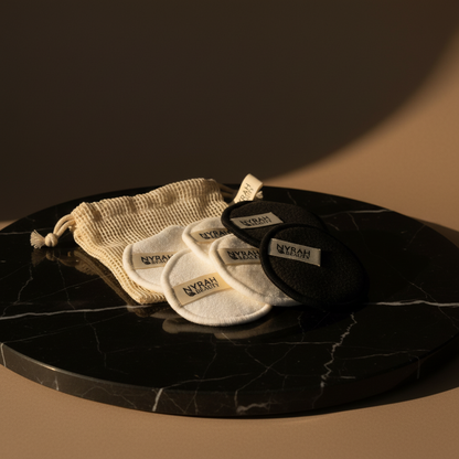 Set of black and white makeup remover pads with a beige drawstring bag on a dark marble surface.