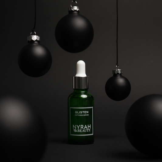 Nyrah Beauty green serum 30ml bottle with black Christmas ornaments on a dark background