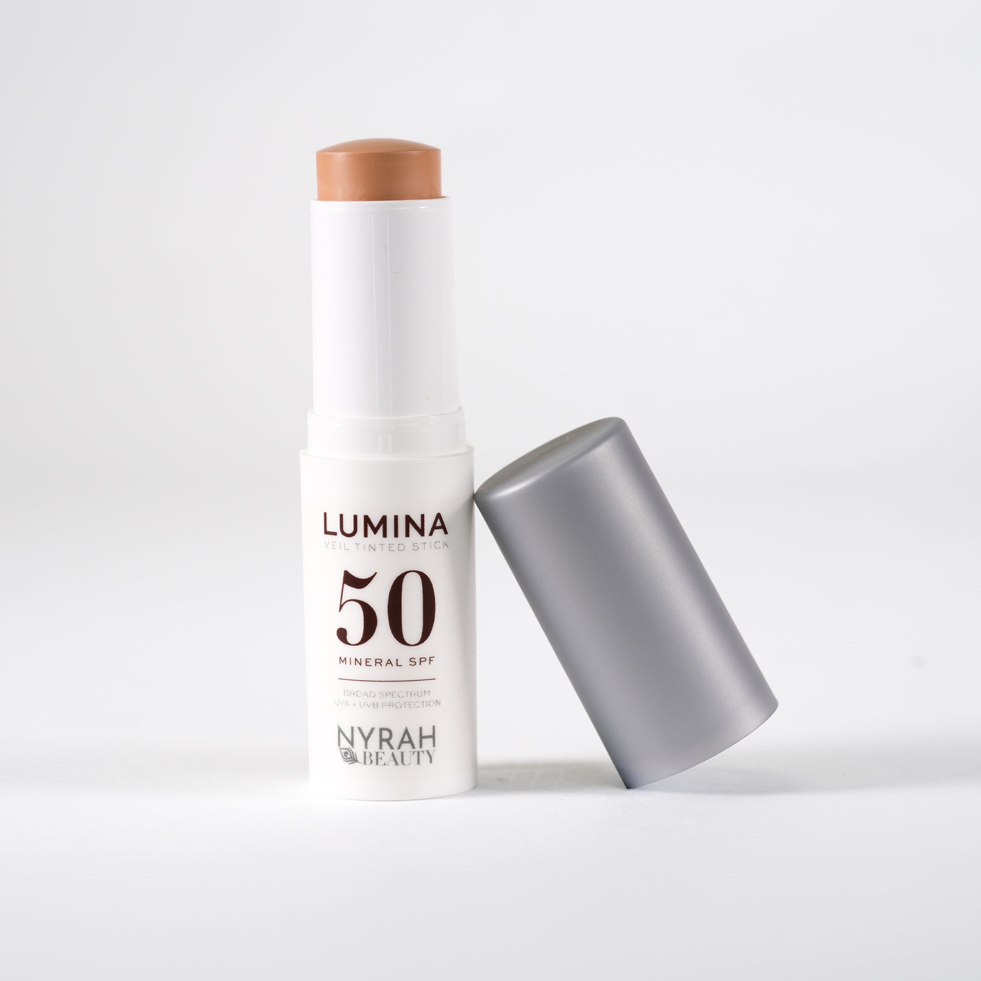 A white stick sunscreen bottle labeled 'LUMINA 50 MINERAL SPF' with a silver cap leaning beside it on a light gray background.